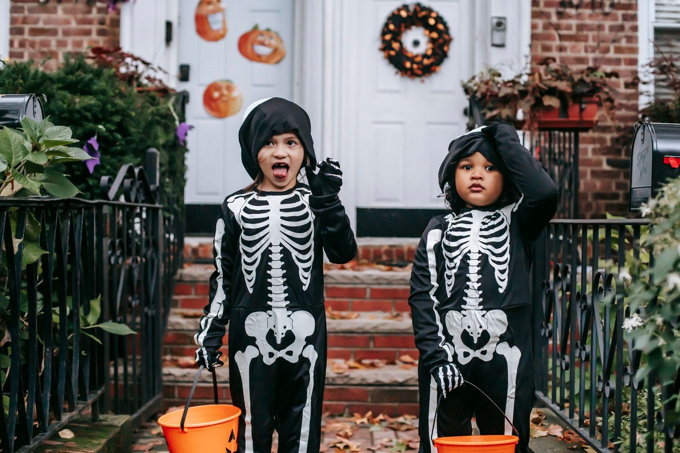 Two children in skeleton Halloween costumes carrying orange trick-or-treat buckets on a porch, used here as a representative image