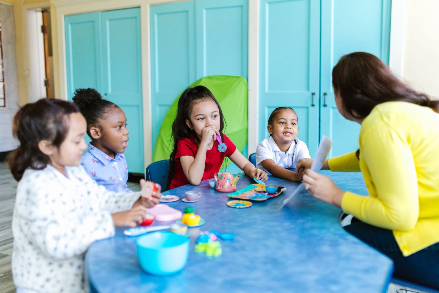 A preschool teacher sits with a small group of young children in a bright, colorful classroom, representative of the pre-K classes now underway at Gwinnett's new Joyful Learning Academy